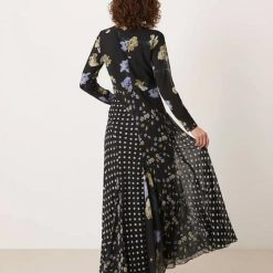 robes longues noires à pois imprimé fleuri col nageur avec manches ourlet godets vue de dos portée par un mannequin aux cheveux bouclés avec des talons noirs