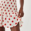 robes vintages rouges à pois froncée basse courte taille sur fond crème- portée par une femme tenant le bas de la jupe