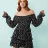 robes asymétriques à pois courte dénudées épaules double épaisseur tissu godets une jeune femme porte une robe noire à pois blancs avec des manches longues et des volants les épaules sont dénudées sur fond bleu clair
