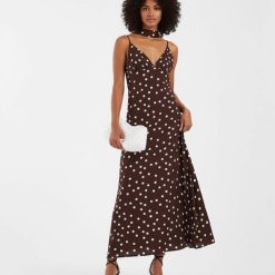 robes évasées à pois longue avec col foulard blanc chocolat portée par une femme avec pochette blanche et talons noirs