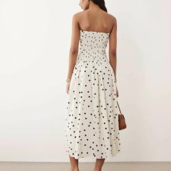 robes évasées à pois fronces bandeau mi longue crème imprimé portee par un mannequin sur un fond bleu pastel