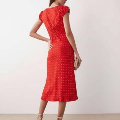 robes longues à pois rouge fluide col v avec mancherons vue de dos portée par un mannequin avec des sandales beige et une pochette