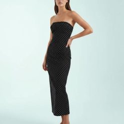 robes longues noires à pois bandeau design moulante sans bretelles ajustée coupe droite portée par un mannequin sur fond bleu clair