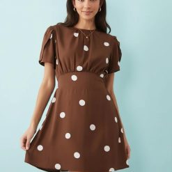 robes longues marron à pois et manches courtes portée par une femme sur un fond bleu clair