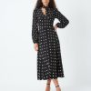 robes longues noires à pois blancs sadie col lavallière longueur mollet à manches longues et décolleté en v portée par un mannequin avec des sandales à talons noirs