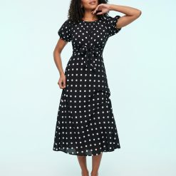 robes longues noires à pois bouffantes manches coupée biais portée par une femme avec une ceinture nouée à la taille et des sandales marron
