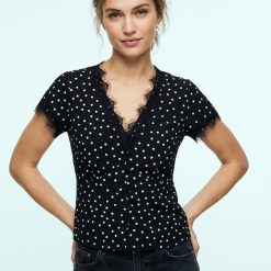 blouses à pois dentelle bordée de design noir portée par une femme avec un jean bleu foncé et un sac noir