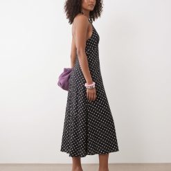 robes longues noires à pois dos nu lynette portée par une femme aux cheveux bouclés avec des sandales noires