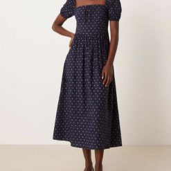 robes à pois transparentes encolure carrée manches bouffantes longueur mollet bleu marine roses portée par une femme avec des chaussures grises sur fond neutre
